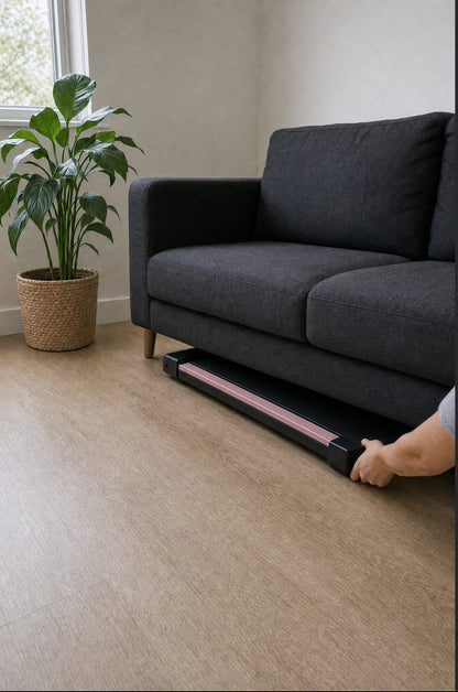 Pink under-desk walking pad being slid flat under a sofa for storage