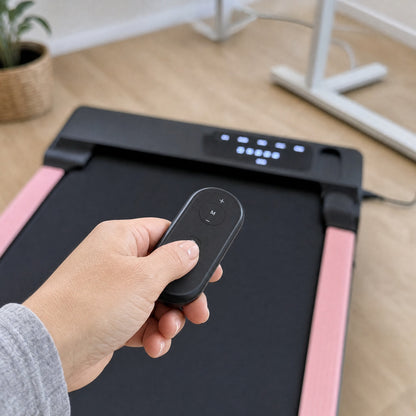 Hand holding the remote control in front of the pink walking pad's LED display