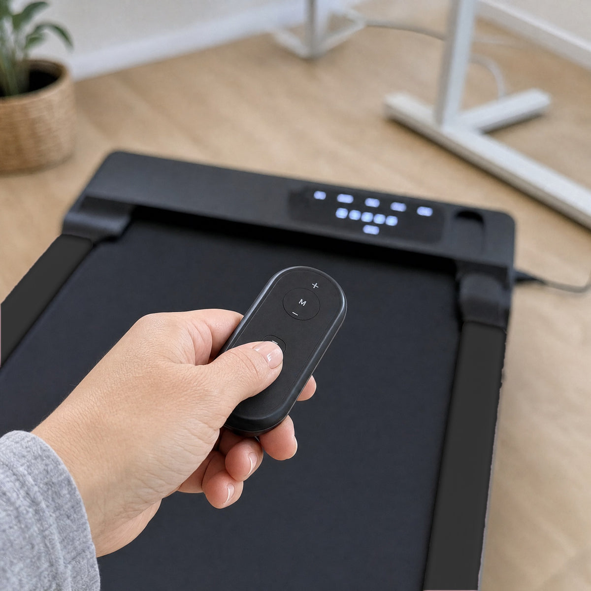 Hand holding the remote control in front of the black walking pad's LED display